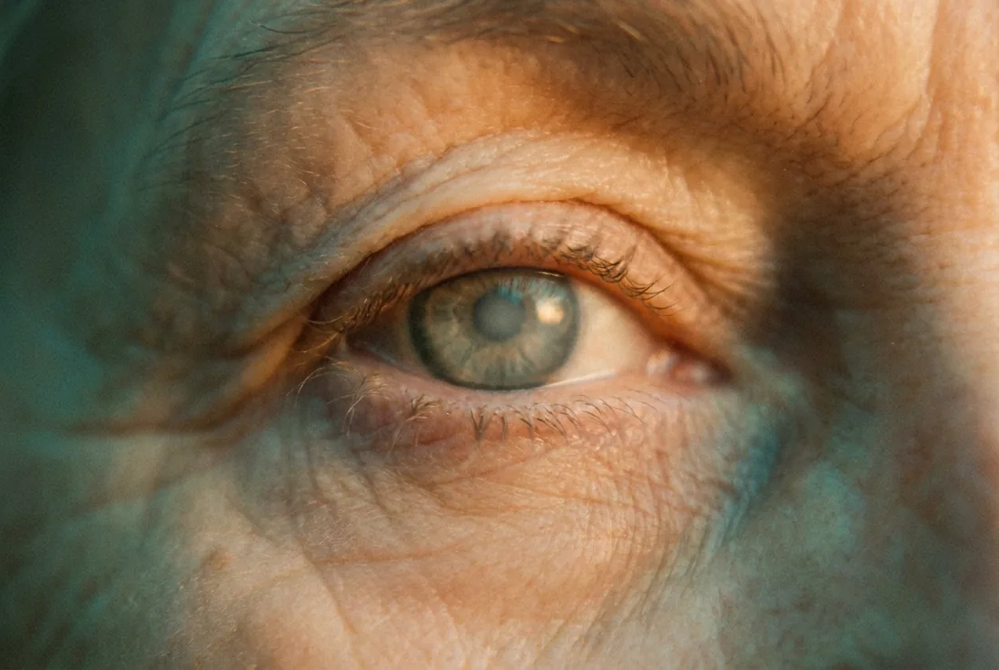 Close-up of an older adult's eye in warm light, with a faint cloudiness over the lens