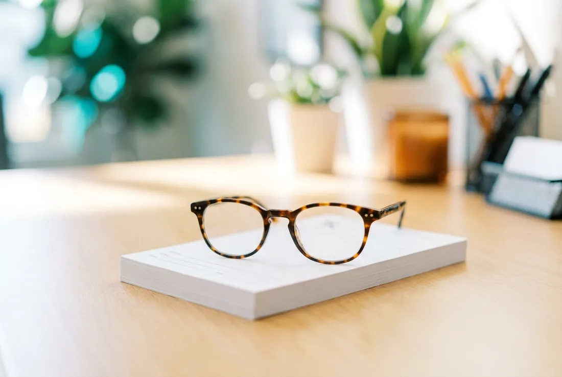 Tortoiseshell reading glasses resting on a neat stack of paper forms on a bright front desk