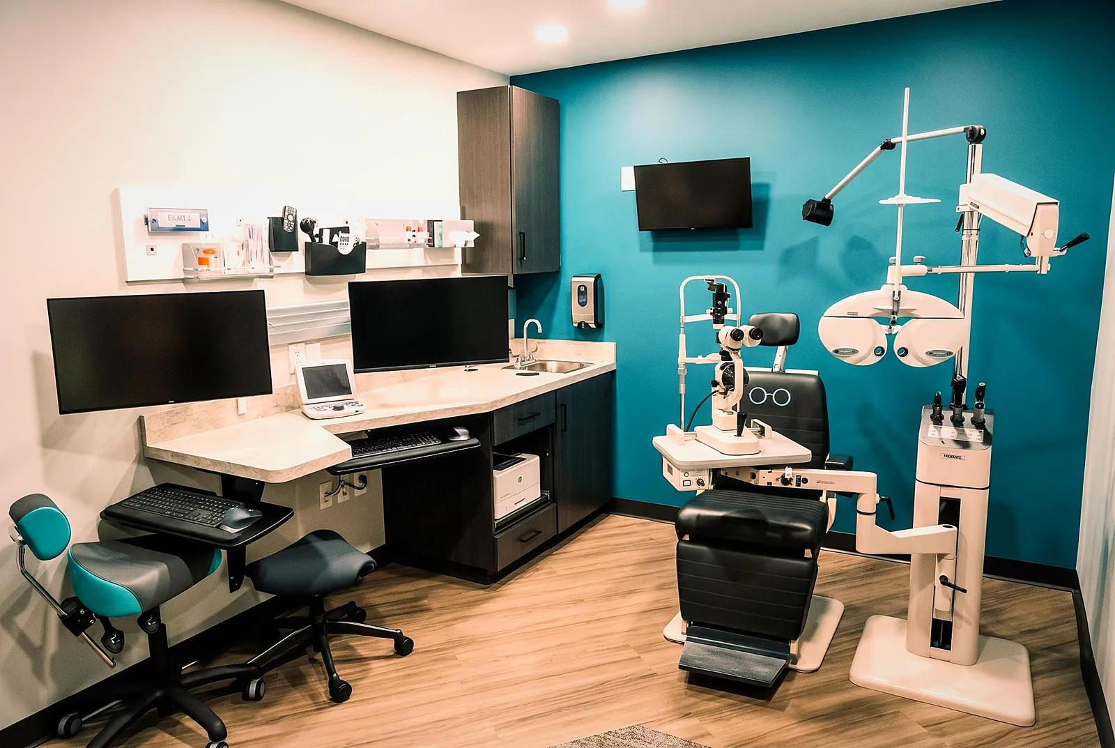 An exam room with the phoropter, exam chair and instruments against the teal accent wall — where your doctor examines the health of your eyes