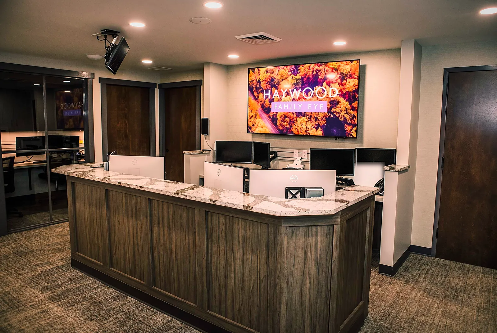 The Haywood Family Eye Care front desk — a granite reception counter beneath the practice's autumn-foliage sign, where you check in